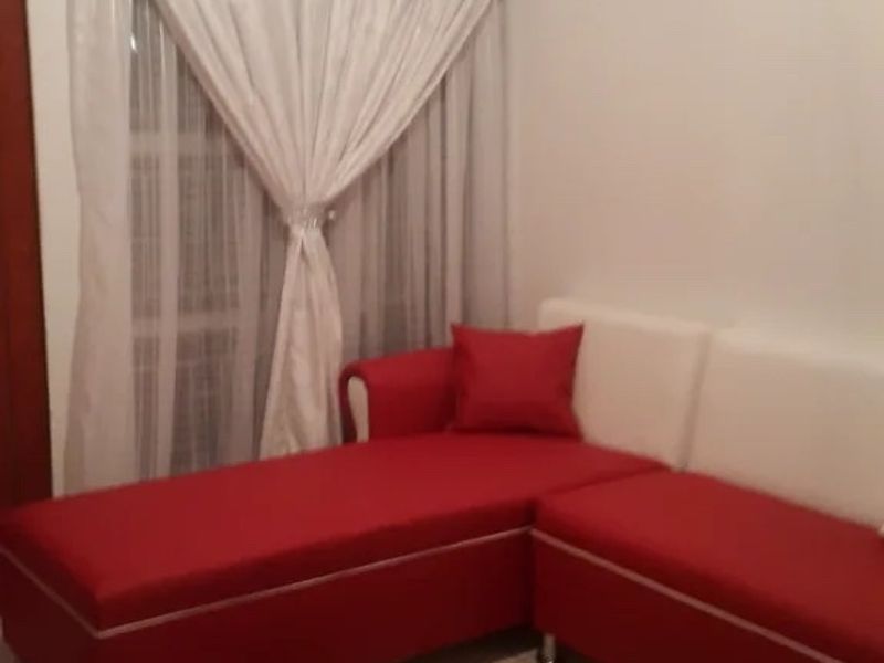 A living room area featuring neutral tiled flooring and a window fitted with a curtain rail.
