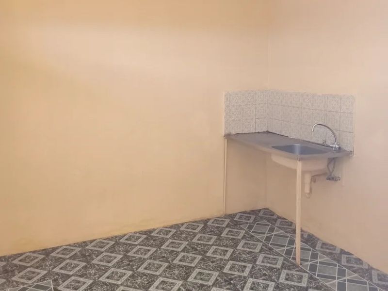 A basic, empty kitchen area featuring a single stainless steel sink with a tiled splashback and patterned floor tiles.