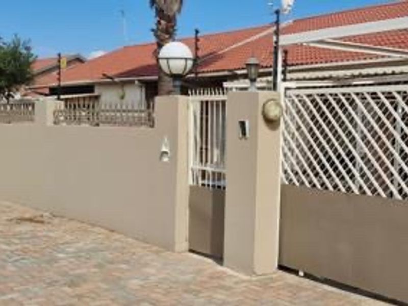 Front exterior view of the property featuring a paved driveway, secure perimeter wall with electric fencing, and gated access.