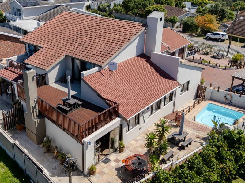 Aerial view of a residential property featuring a tiled roof, elevated wooden deck, swimming pool, and paved outdoor entertainment area.