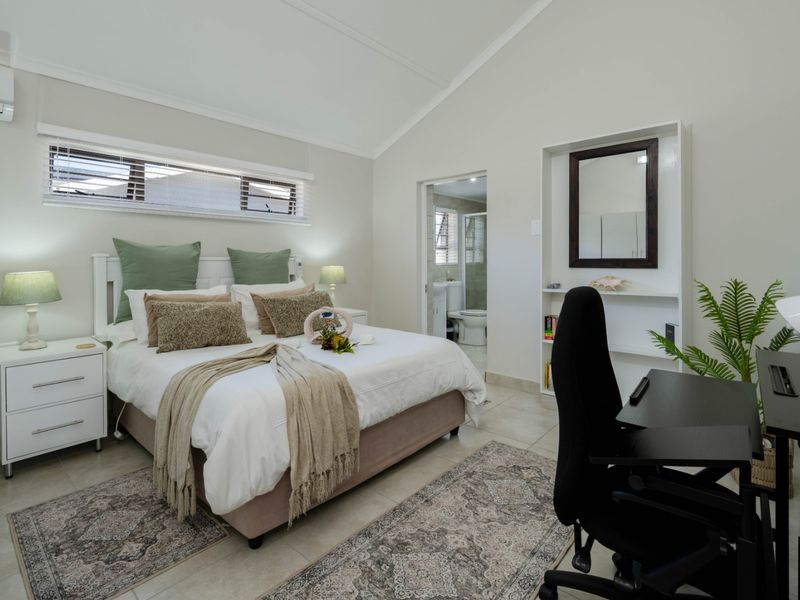 Spacious bedroom featuring a vaulted ceiling, tiled flooring, split-system air conditioning, and convenient en-suite bathroom access.