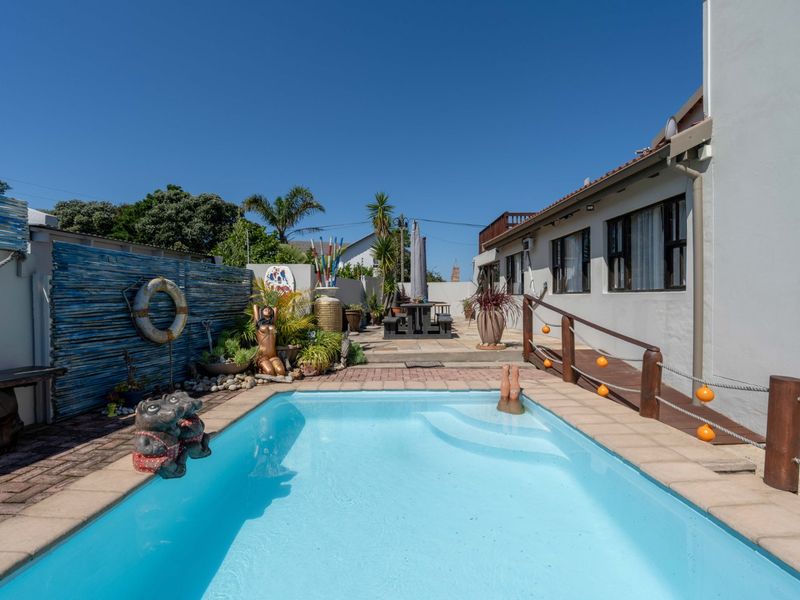 Outdoor pool area featuring a swimming pool with paved surround, timber decking, and a wooden handrail, set against a private boundary wall.