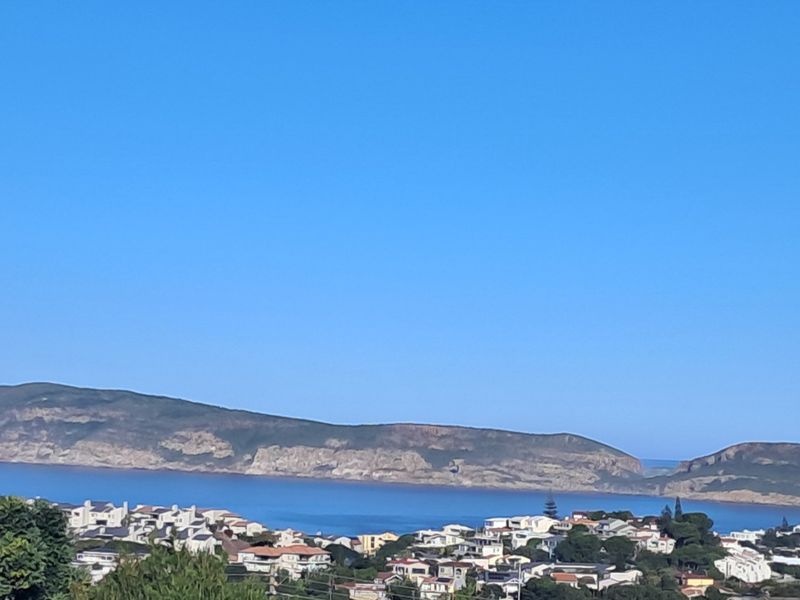 A scenic elevated view overlooking the coastal residential area and the ocean with distant hills in the background.