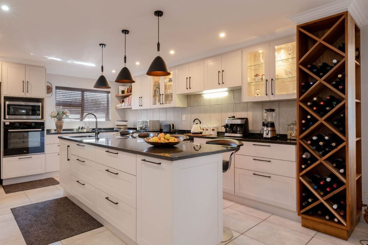 Modern kitchen featuring a central island, granite countertops, built-in appliances, and a custom integrated wine rack, finished with neutral cabinetry and tiled flooring.