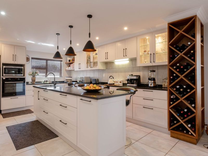 Modern kitchen featuring a central island, granite countertops, built-in appliances, and a custom integrated wine rack, finished with neutral cabinetry and tiled flooring.