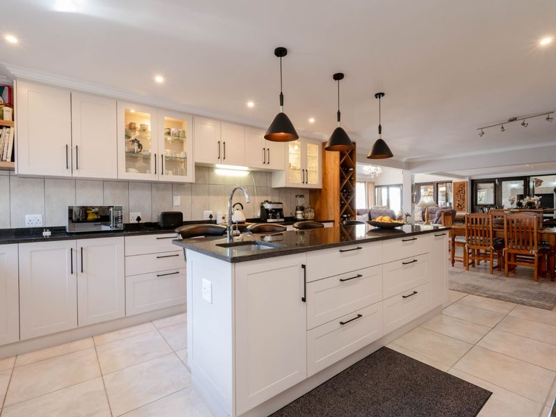 Spacious open-plan kitchen featuring a large central island, granite countertops, modern shaker cabinetry, and integrated lighting, flowing seamlessly into the dining and living areas.