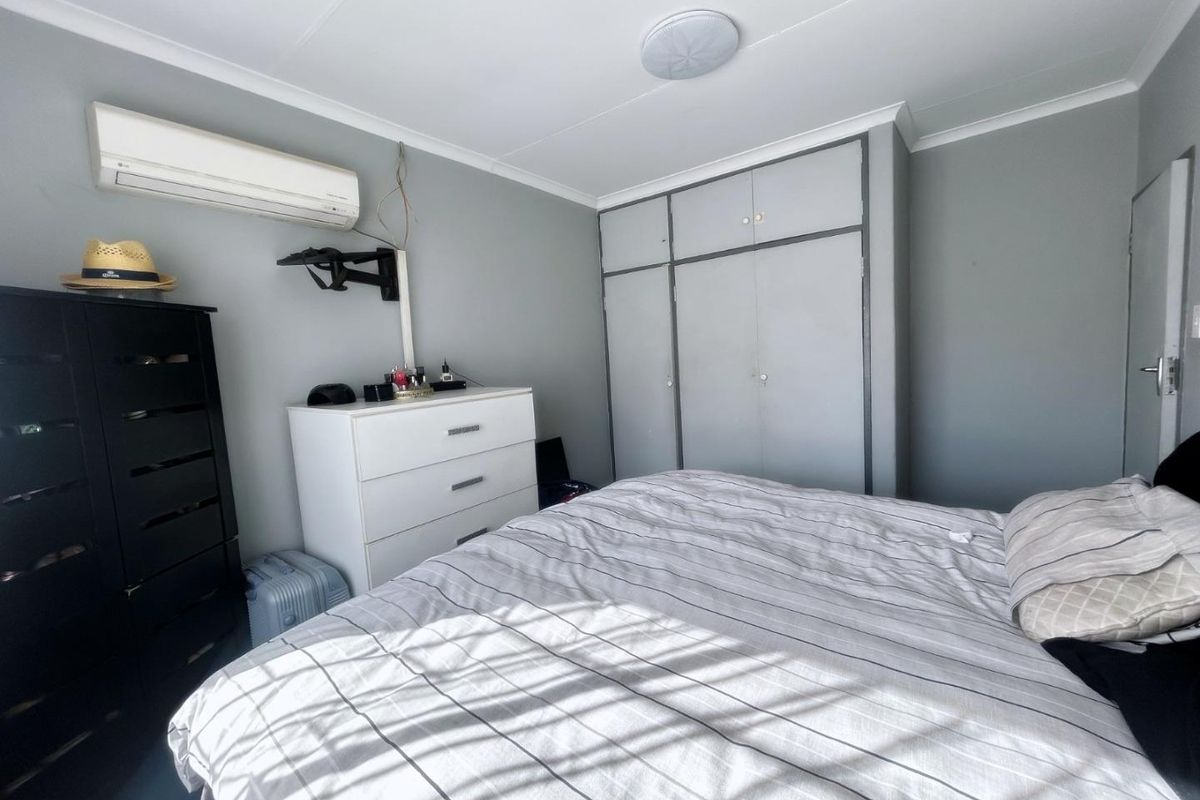 A bedroom featuring built-in cupboards, an air conditioning unit, and neutral wall finishes.