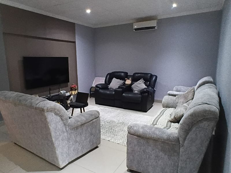 A comfortable living room featuring tiled flooring, recessed downlighting, and a wall-mounted split-system air conditioning unit.