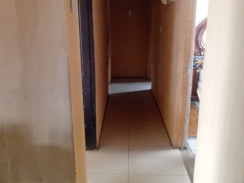 A narrow residential hallway featuring tiled flooring and multiple internal doorways, currently requiring ceiling repairs and cosmetic updates.