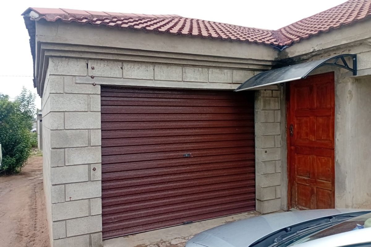 Exterior view of a garage featuring a roller shutter door, concrete block construction, and a timber entrance door with a protective canopy.