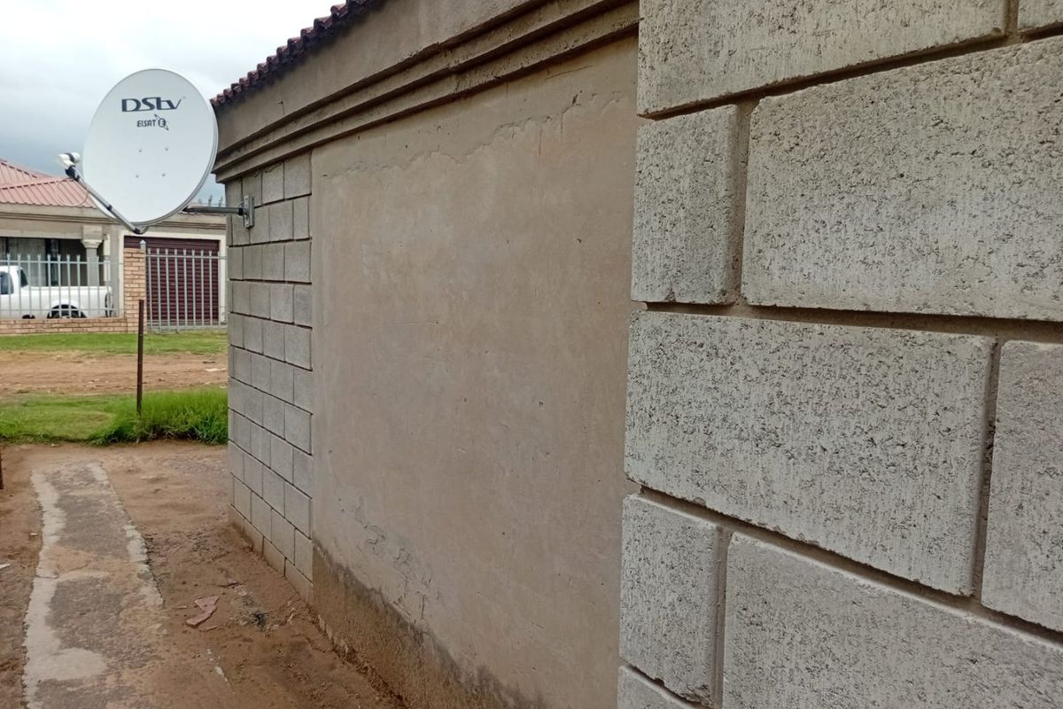 A view of the exterior side wall featuring concrete block construction, a satellite dish, and visible signs of damp and plaster wear at the base.