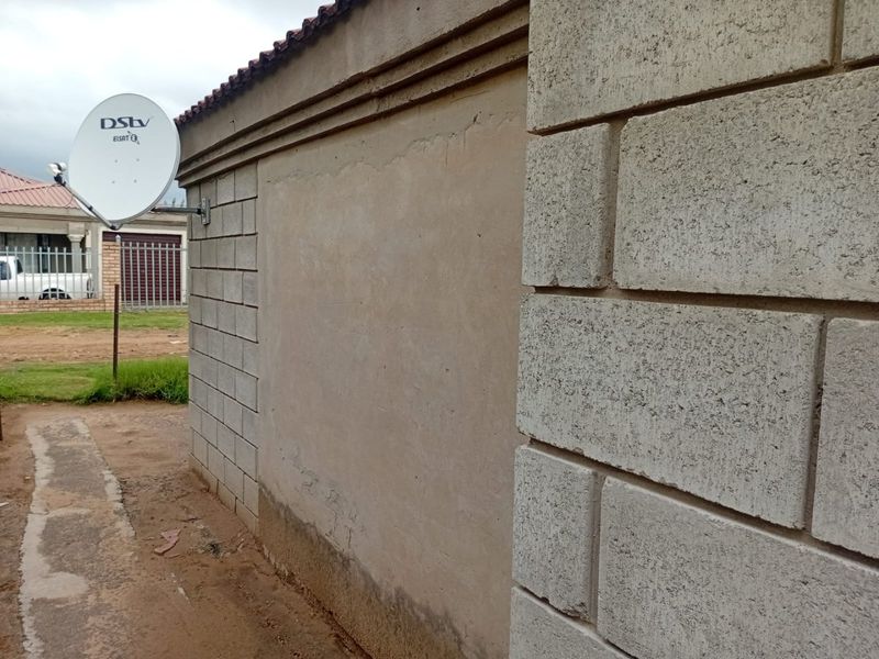 A view of the exterior side wall featuring concrete block construction, a satellite dish, and visible signs of damp and plaster wear at the base.