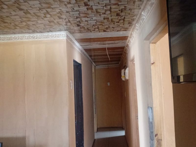 A narrow hallway featuring decorative ceiling tiles, crown molding, and tiled flooring, requiring cosmetic updates to improve the overall aesthetic.