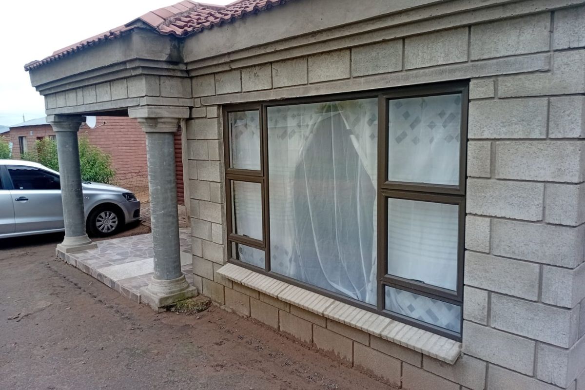 Front facade of a house featuring concrete block masonry, a covered porch with decorative columns, and aluminium window frames.