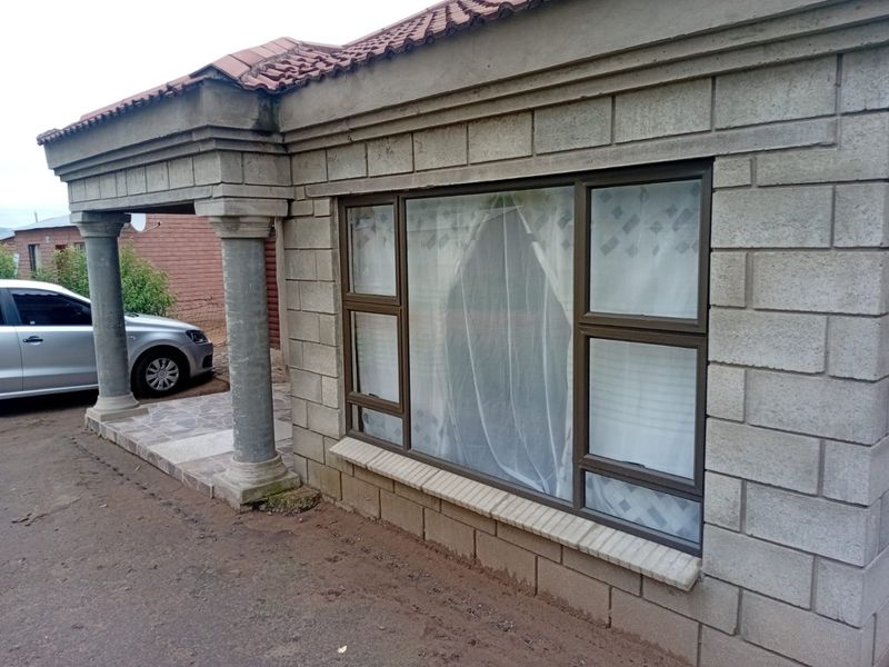 Front facade of a house featuring concrete block masonry, a covered porch with decorative columns, and aluminium window frames.
