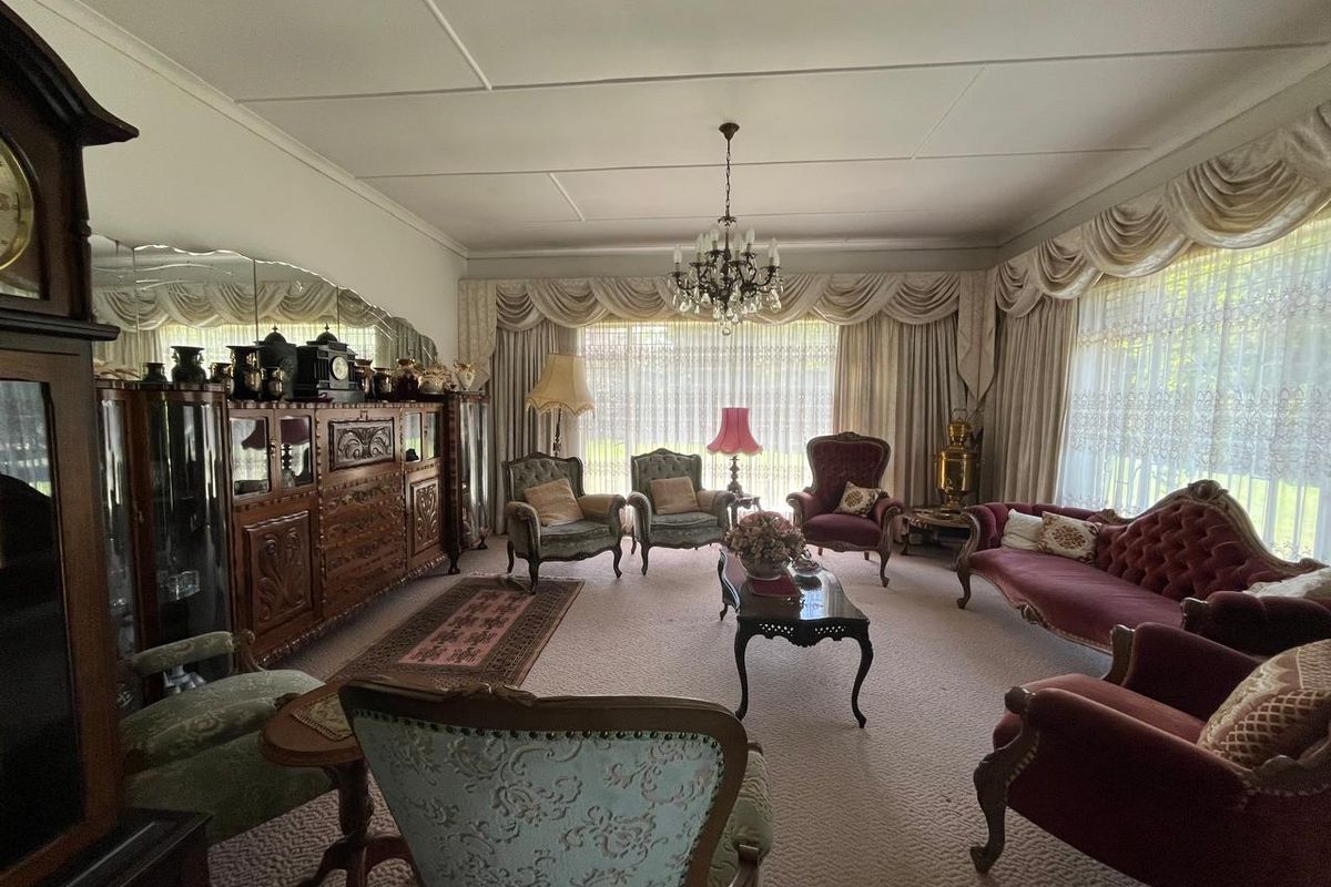Spacious formal living room featuring a classic chandelier, wall-to-wall carpeting, and large windows with decorative drapery.