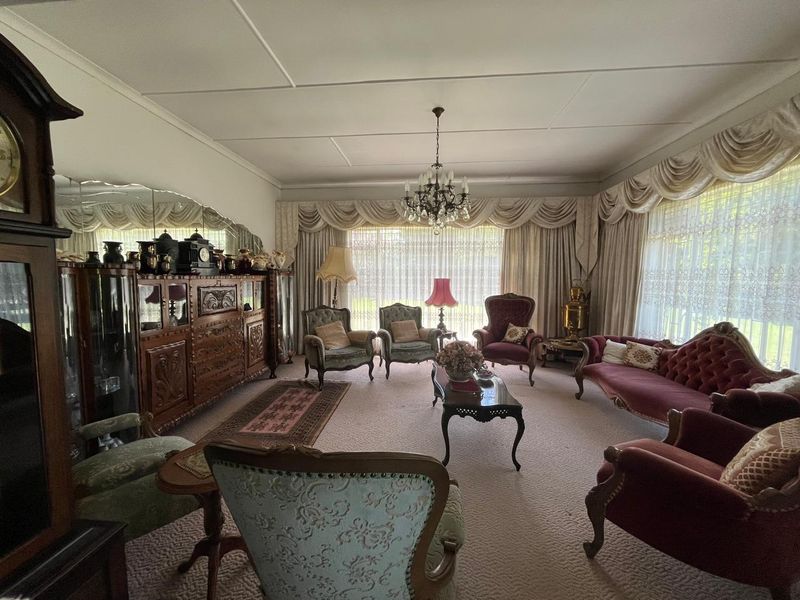 Spacious formal living room featuring a classic chandelier, wall-to-wall carpeting, and large windows with decorative drapery.