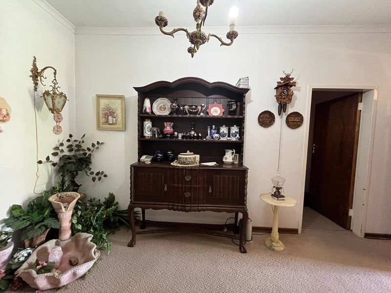 A living area featuring carpeted flooring, an ornate chandelier, and a wall-mounted light fixture, providing a traditional foundation for interior updates.