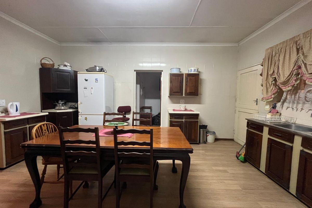 A functional kitchen featuring dark wood cabinetry, laminate flooring, and a tiled splashback, offering a practical layout with ample storage space.