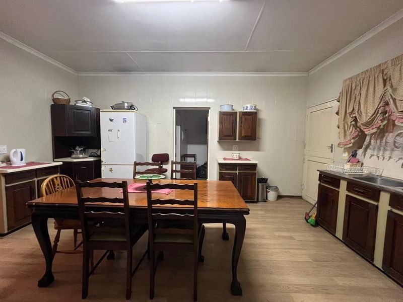 A functional kitchen featuring dark wood cabinetry, laminate flooring, and a tiled splashback, offering a practical layout with ample storage space.