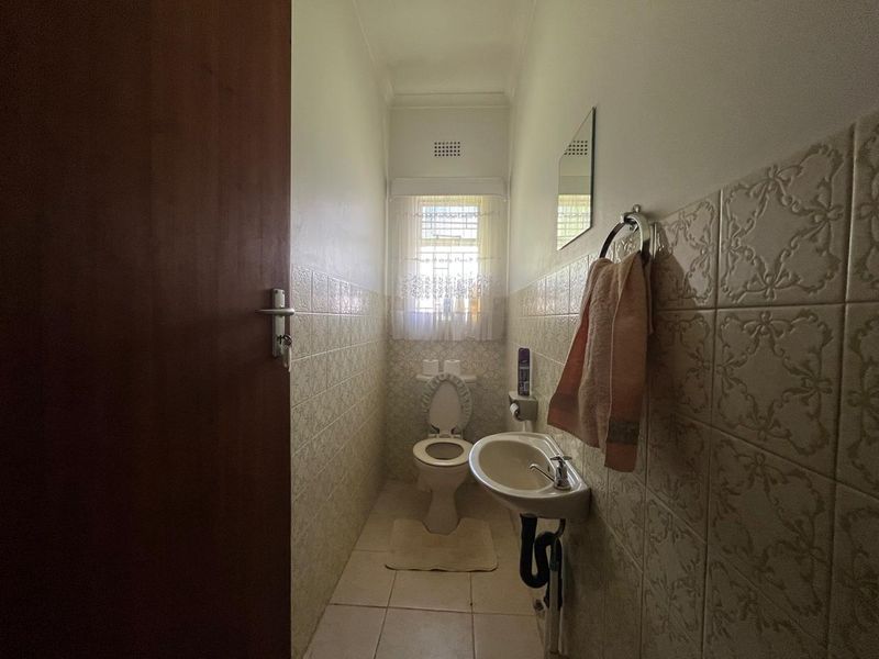 A compact guest bathroom featuring tiled walls, a wall-mounted basin, and a standard toilet, offering a functional layout in a neutral finish.