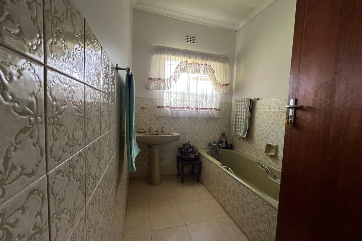 A dated bathroom featuring a pedestal basin, built-in bathtub, and traditional tiled finishes throughout.