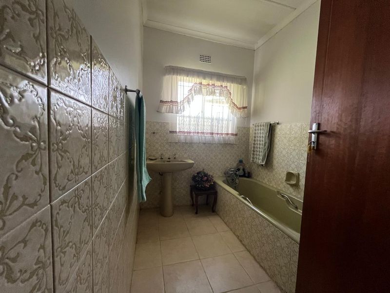 A dated bathroom featuring a pedestal basin, built-in bathtub, and traditional tiled finishes throughout.
