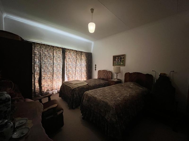 A bedroom featuring neutral walls and large window curtains, providing a functional space with potential for modernization.