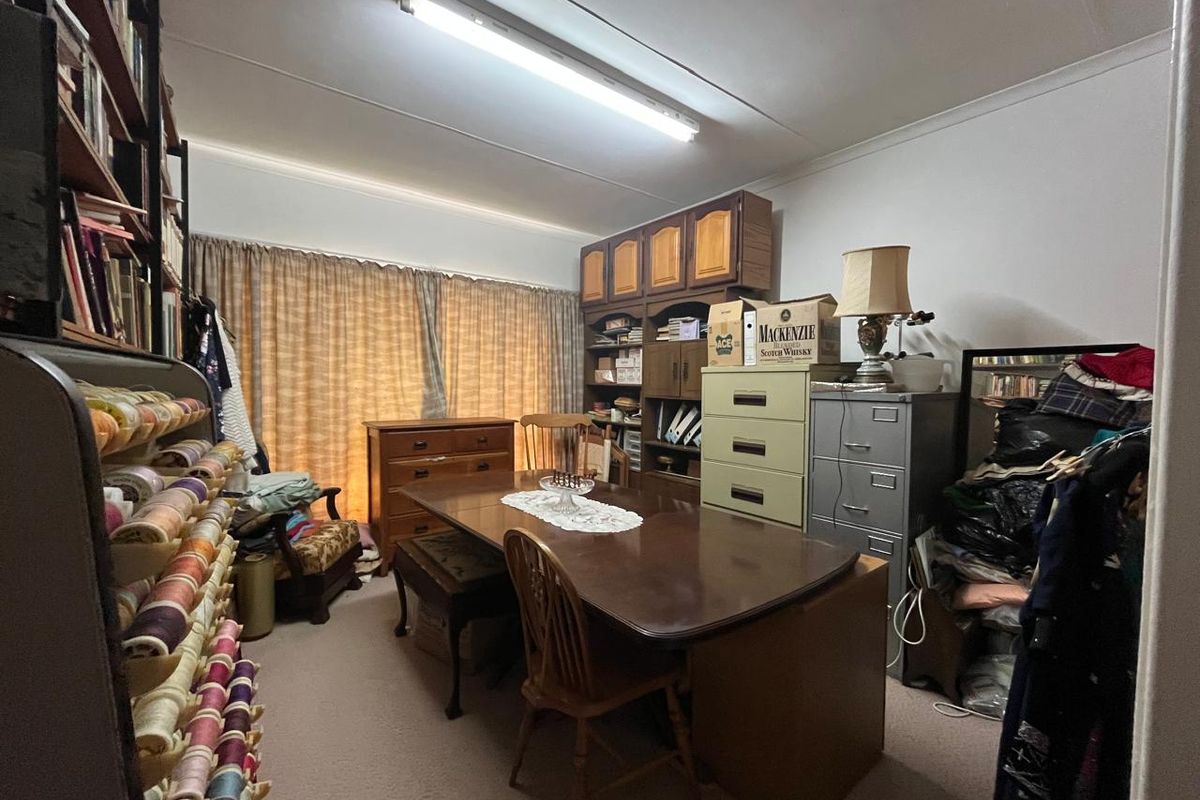 A multi-purpose room currently used as a study or hobby space, featuring built-in cabinetry and fluorescent lighting.