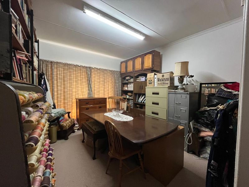 A multi-purpose room currently used as a study or hobby space, featuring built-in cabinetry and fluorescent lighting.