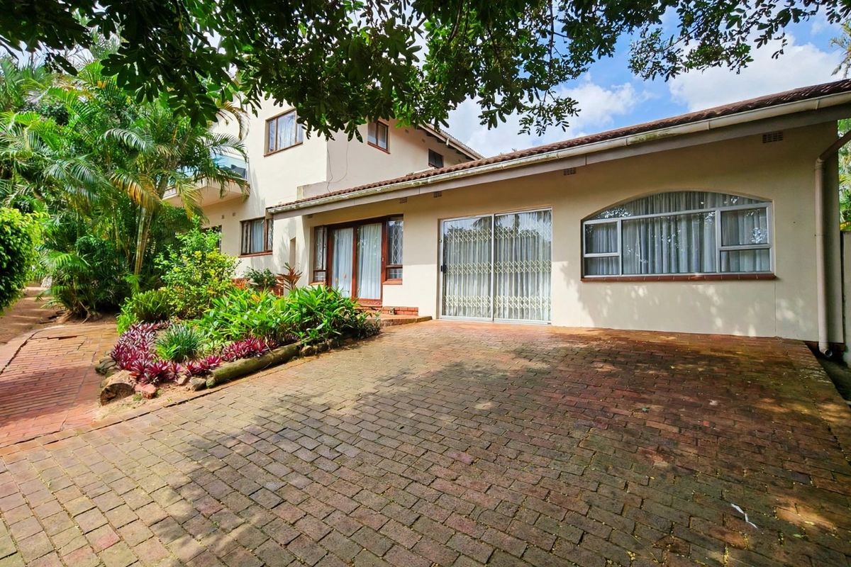 Rear exterior view of the property featuring a brick paved patio area, established garden, and sliding glass doors with security gates.