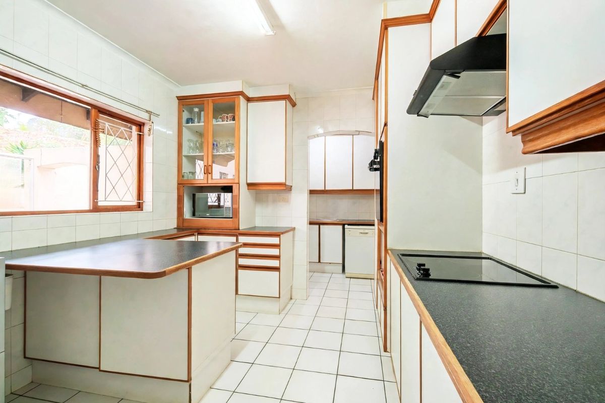 A functional kitchen featuring white cabinetry with wood trim, dark laminate countertops, an electric hob, and tiled flooring throughout.
