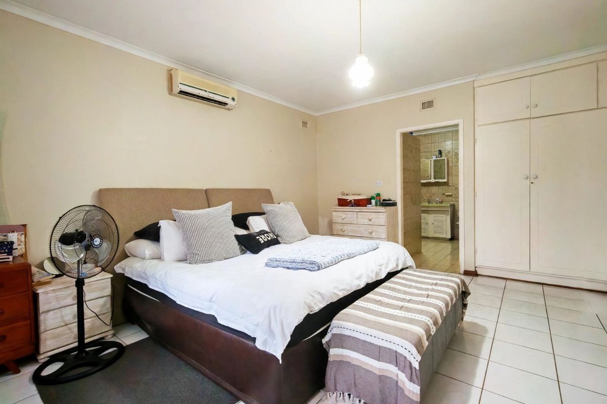 Spacious bedroom featuring tiled flooring, built-in cupboards, and an air conditioning unit, with an adjoining en-suite bathroom.
