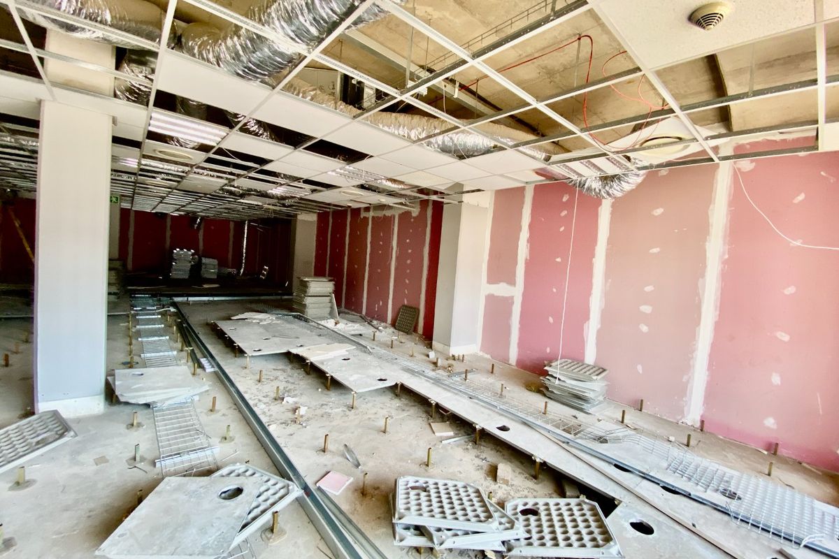 An unfinished commercial interior space featuring exposed ductwork, a suspended ceiling grid, and raised access flooring, currently undergoing renovation or fit-out.