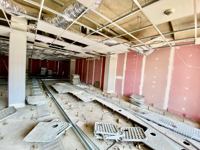 An unfinished commercial interior space featuring exposed ductwork, a suspended ceiling grid, and raised access flooring, currently undergoing renovation or fit-out.