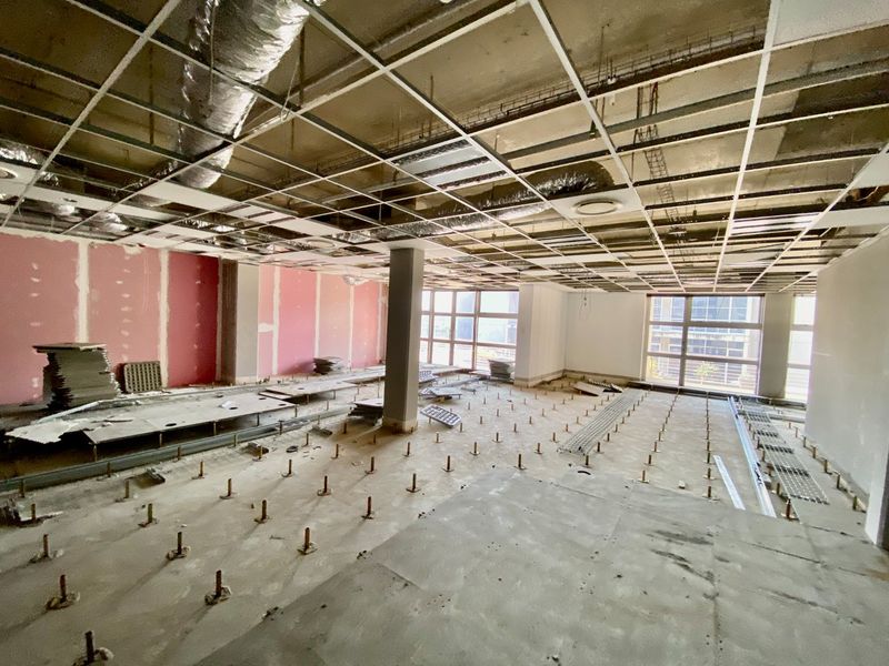 A large, open-plan commercial office space currently under renovation, featuring exposed ceiling grids, HVAC ducting, and raised floor pedestals ready for final fit-out.