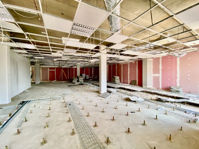 An open-plan commercial office space currently undergoing renovation, featuring exposed ceiling infrastructure, raised floor pedestals, and unfinished drywall partitions.