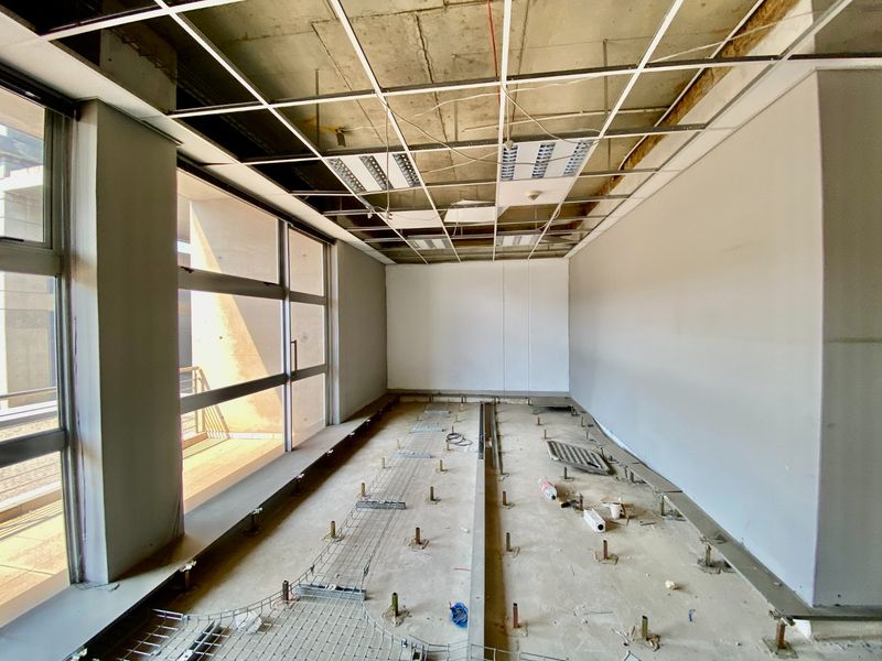 Unfinished commercial office space featuring a raised access floor system, exposed ceiling grid, and large windows providing natural light.