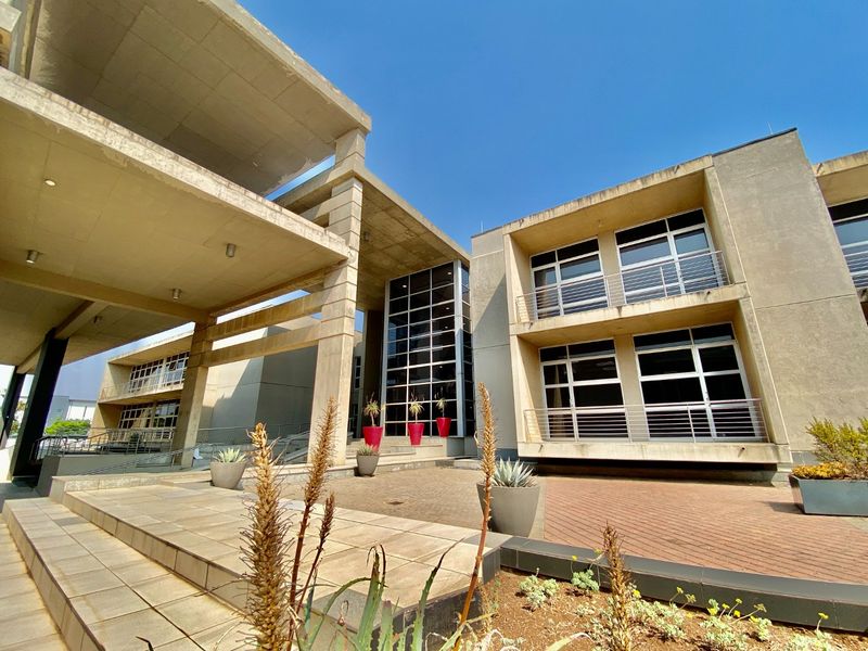 Modern commercial building exterior featuring a prominent concrete structure, large glass curtain wall, and multi-level balconies with steel railings.