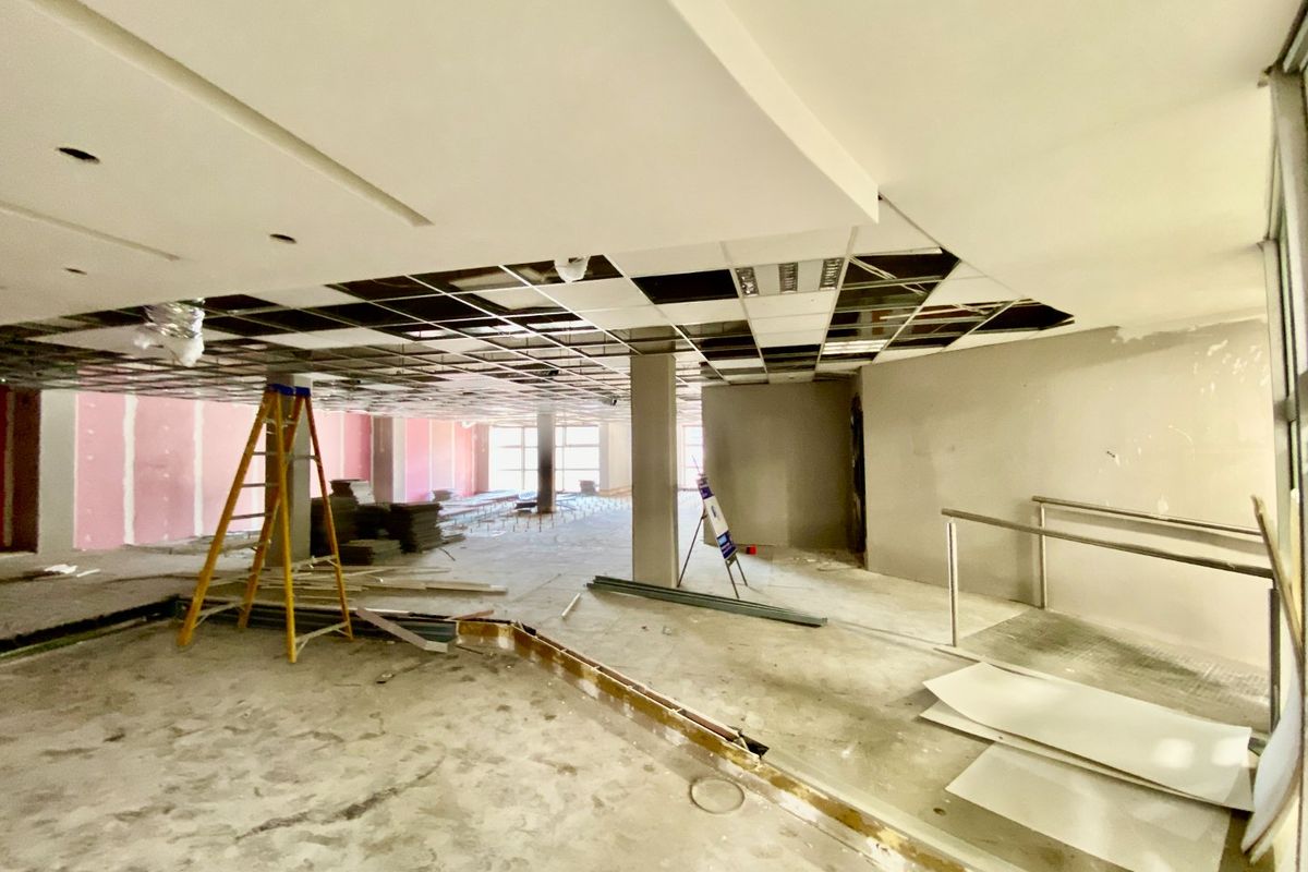A large, open-plan commercial space currently undergoing renovation, featuring exposed ceiling grids, unfinished walls, and structural columns ready for fit-out.
