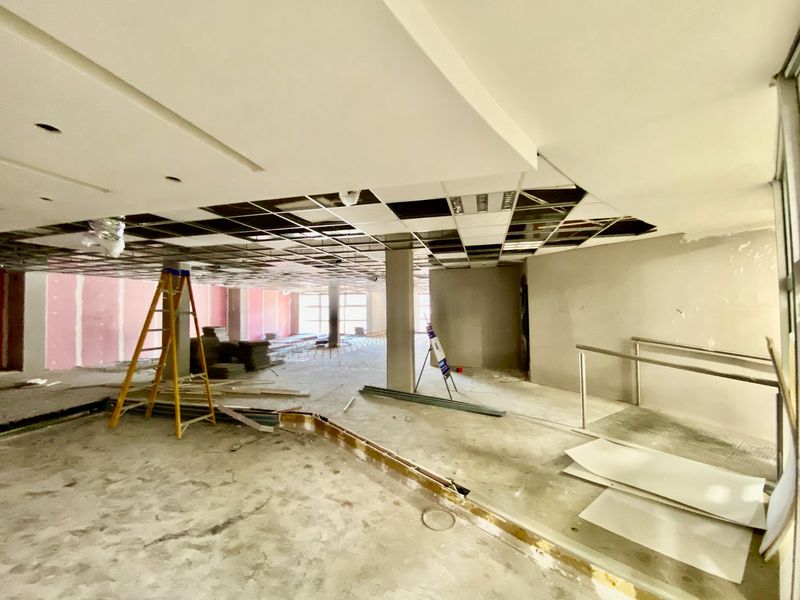 A large, open-plan commercial space currently undergoing renovation, featuring exposed ceiling grids, unfinished walls, and structural columns ready for fit-out.