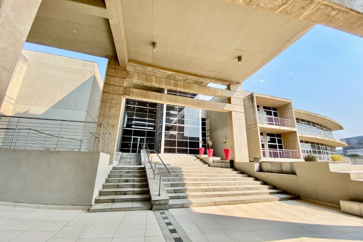 Modern commercial building entrance featuring a prominent concrete structure, expansive glass facade, and wide stone staircase leading to the main entry.