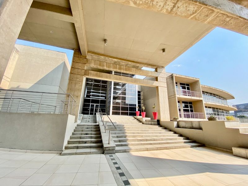 Modern commercial building entrance featuring a prominent concrete structure, expansive glass facade, and wide stone staircase leading to the main entry.