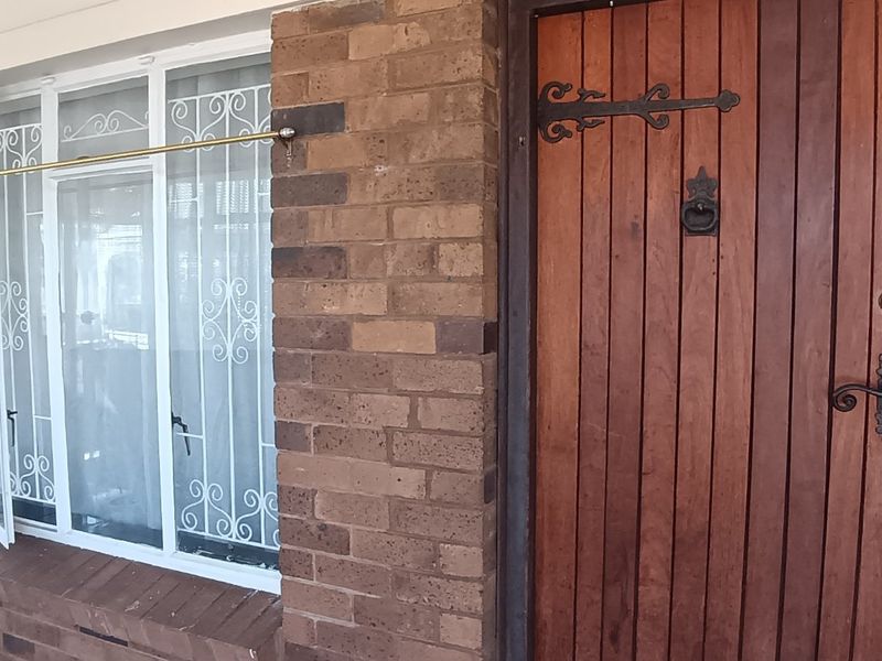 A covered entrance porch featuring a solid timber front door, brick facade, and security-barred windows.
