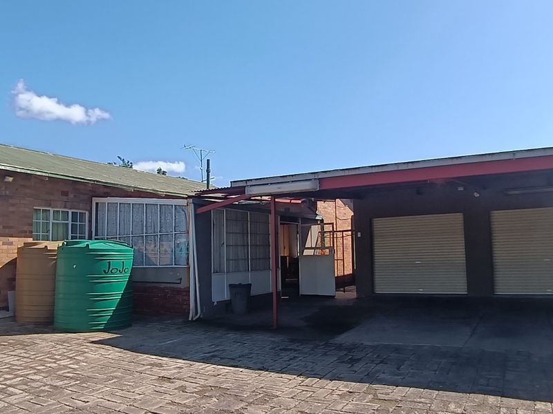 Rear exterior view featuring a paved courtyard, double garage with roller shutter doors, covered carport area, and water storage tanks.