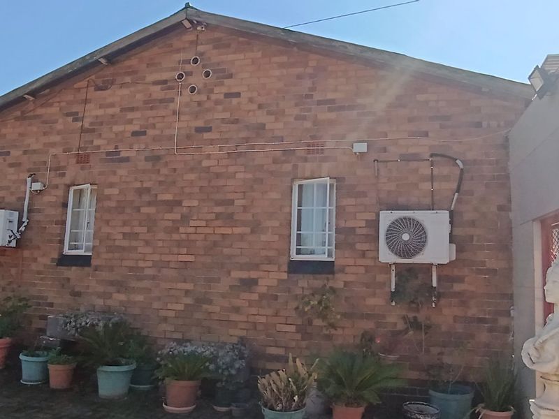 Rear view of the property featuring a face brick facade, installed air conditioning units, security bars on windows, and an external water storage tank.