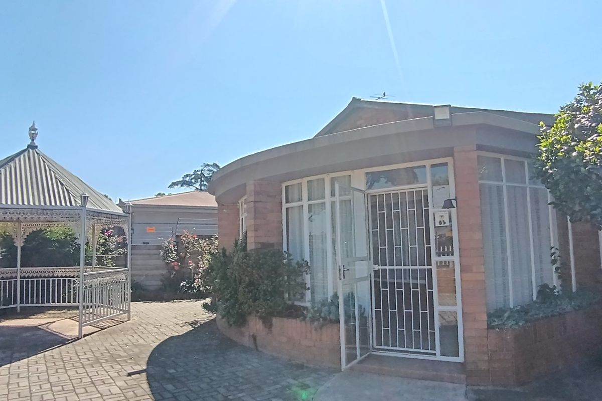 Rear view of the property featuring a brick facade, large windows with security gates, and a paved courtyard area with a metal gazebo.