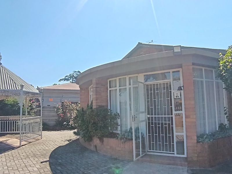 Rear view of the property featuring a brick facade, large windows with security gates, and a paved courtyard area with a metal gazebo.