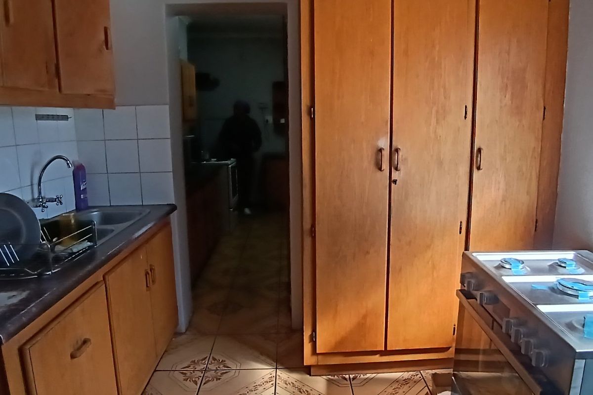 A dated kitchen featuring original wooden cabinetry, tiled backsplash, and a gas stove, offering significant potential for a modern renovation.