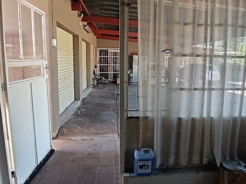 A covered outdoor patio area featuring tiled flooring, security gates, and roller shutter doors, providing a functional transition space between the interior and exterior.